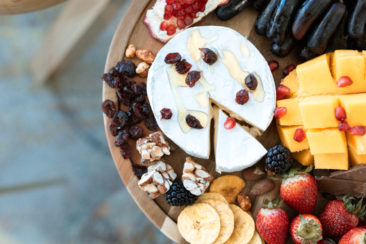 Colorful platter featuring assorted cheese, fruits, and nuts on a wooden board.